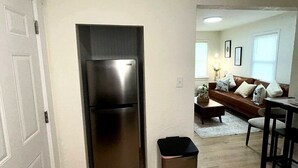 A kitchen with a stainless steel refrigerator, a trash bin, and a wooden floor.