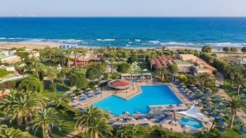 A resort with a central pool, palm trees, and a beach view.
