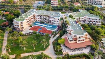 A multi-story hotel with a swimming pool, surrounded by greenery and palm trees.