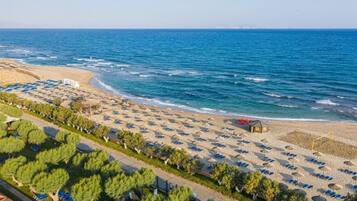 A beach with rows of sun loungers and umbrellas, a sandy shore, and a clear view of the sea.