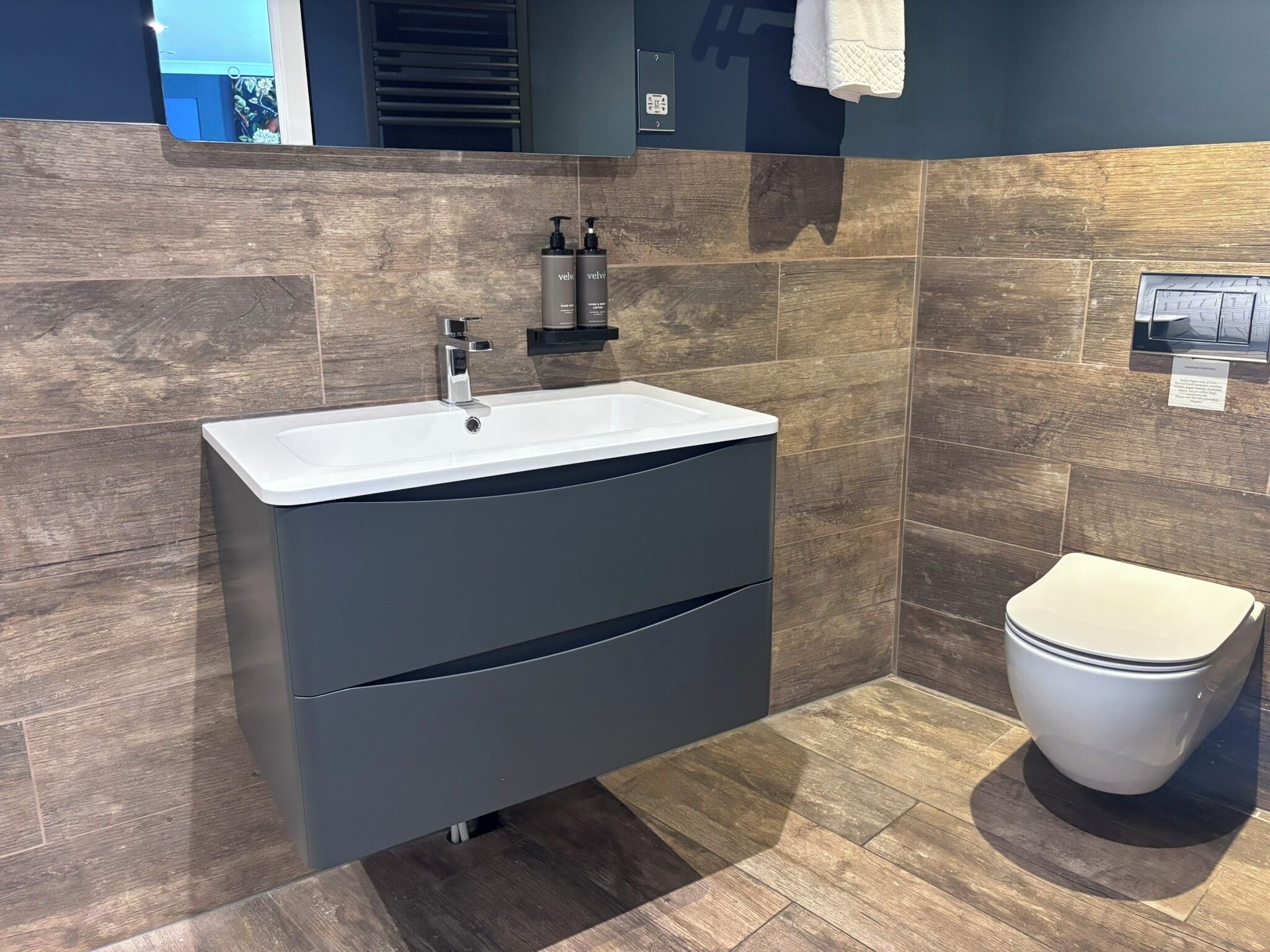 A modern bathroom with a white sink, dark cabinetry, and a toilet.