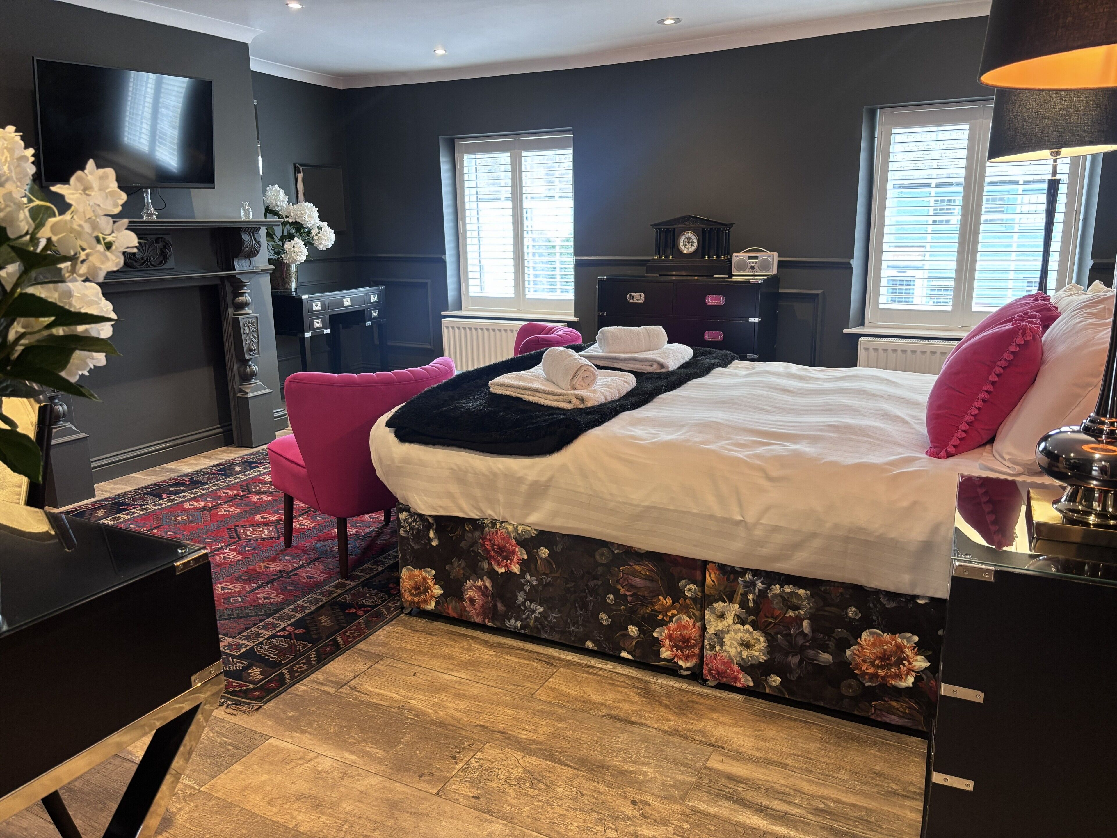 Un dormitorio con cama, televisión, cómoda, silla y escritorio.