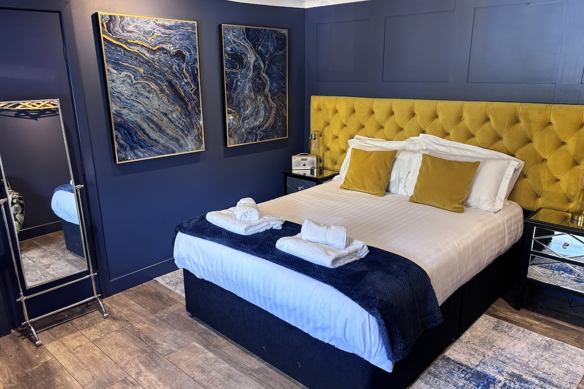 A modern hotel room with a large bed, a yellow tufted headboard, and two abstract paintings on the wall.