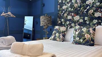 A hotel room with a bed, a mirror, a lamp, and a floral-patterned wall.