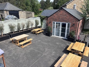 Une terrasse avec des bancs en bois et un bĂątiment en briques dotĂ© dâune porte en verre.