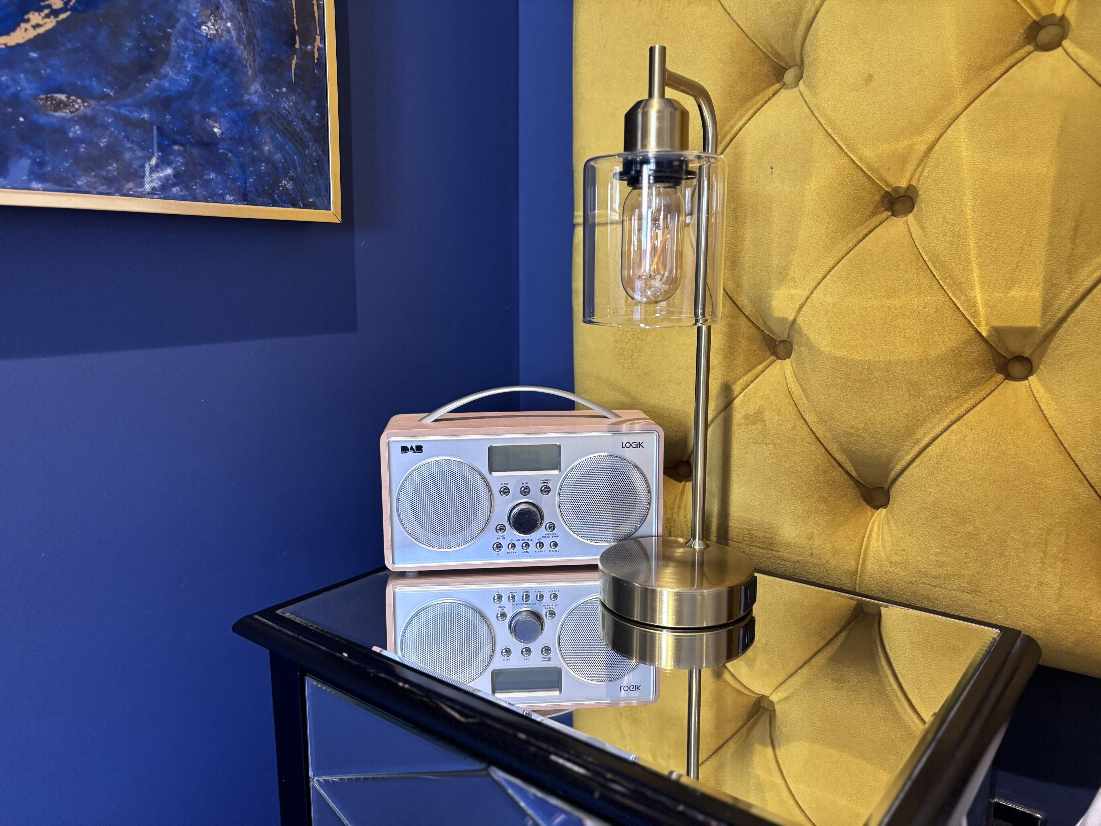 Een radio op een glazen tafel, met een gebobbelde gele hoofdbord op de achtergrond.