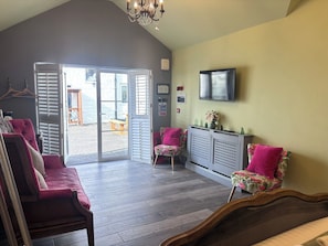 A room with a large sliding glass door leading outside, a flat-screen TV mounted on the wall, and a seating area with a sofa and chairs. - The Old Post Office - B&B and Coffee Shop (Newcastle-upon-Tyne)