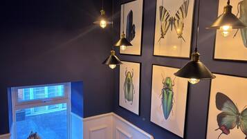A room with a dark wall, multiple framed insect illustrations, and hanging pendant lights.