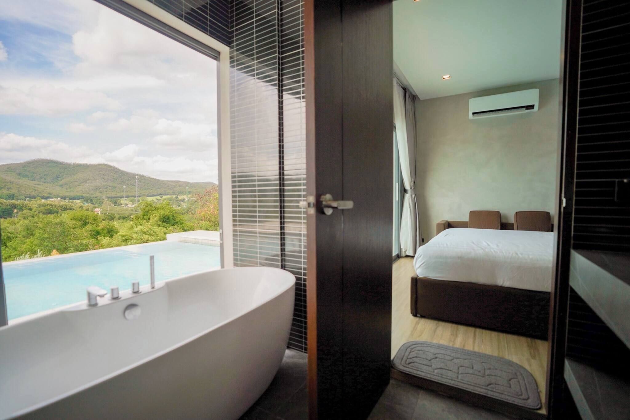 A modern bathroom with a large bathtub, a shower, and a view of a mountainous landscape.