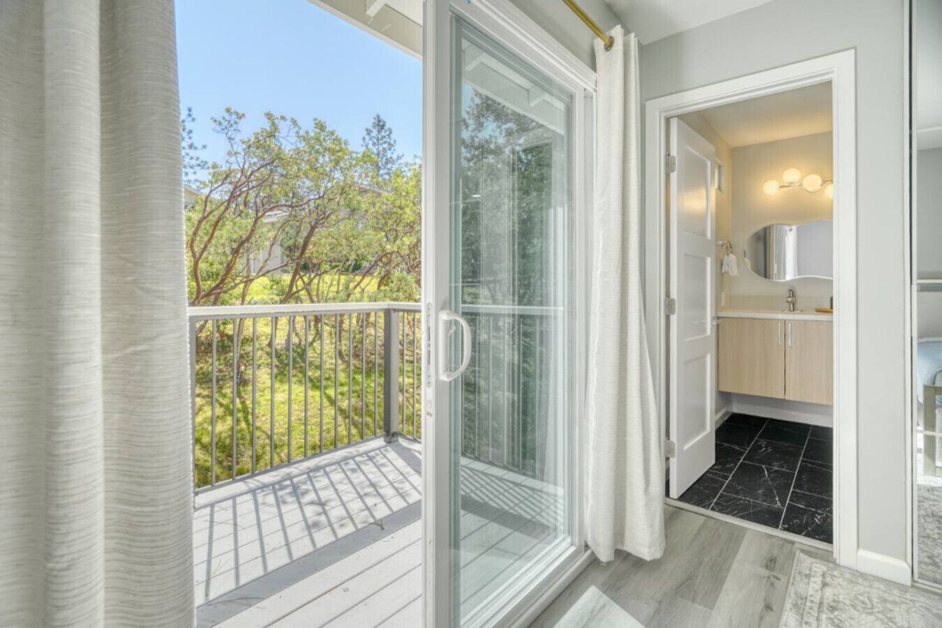 A balcony with a glass door leading to a bathroom with a sink and mirror.