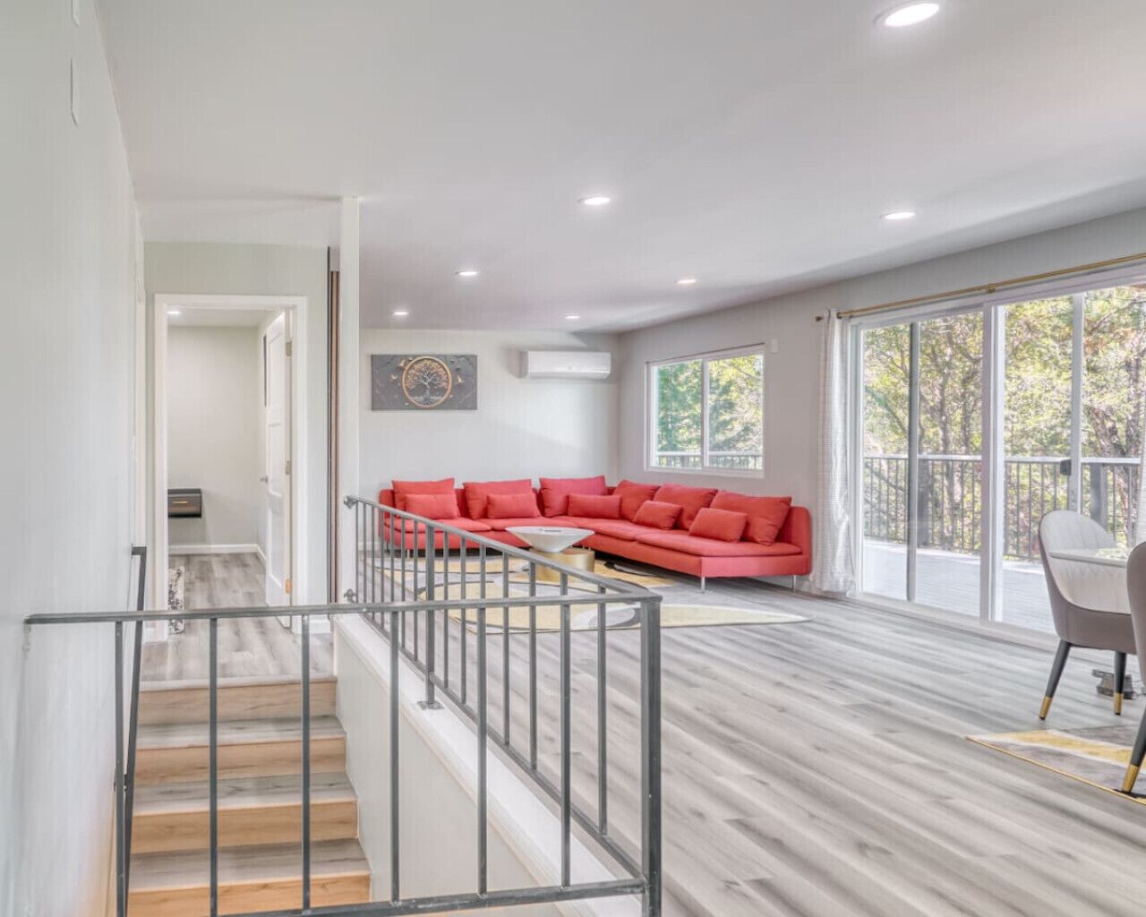 A spacious living area with a red sectional sofa, a dining table, and a staircase.