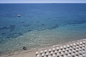 A beach with clear water, a boat, and umbrellas.