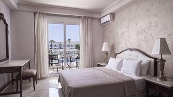 A hotel room with a bed, a desk, a chair, a lamp, and a view of a pool and buildings.