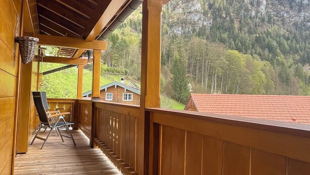 Een houten balkon met uitzicht op een berg en een huis.