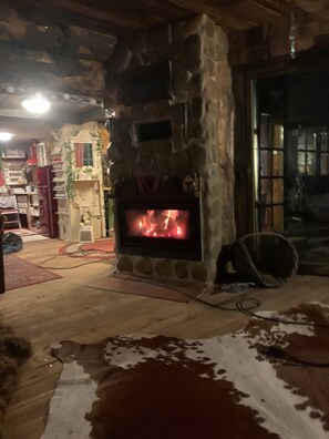 A stone fireplace with a fire, a wooden floor, and a cowhide rug.