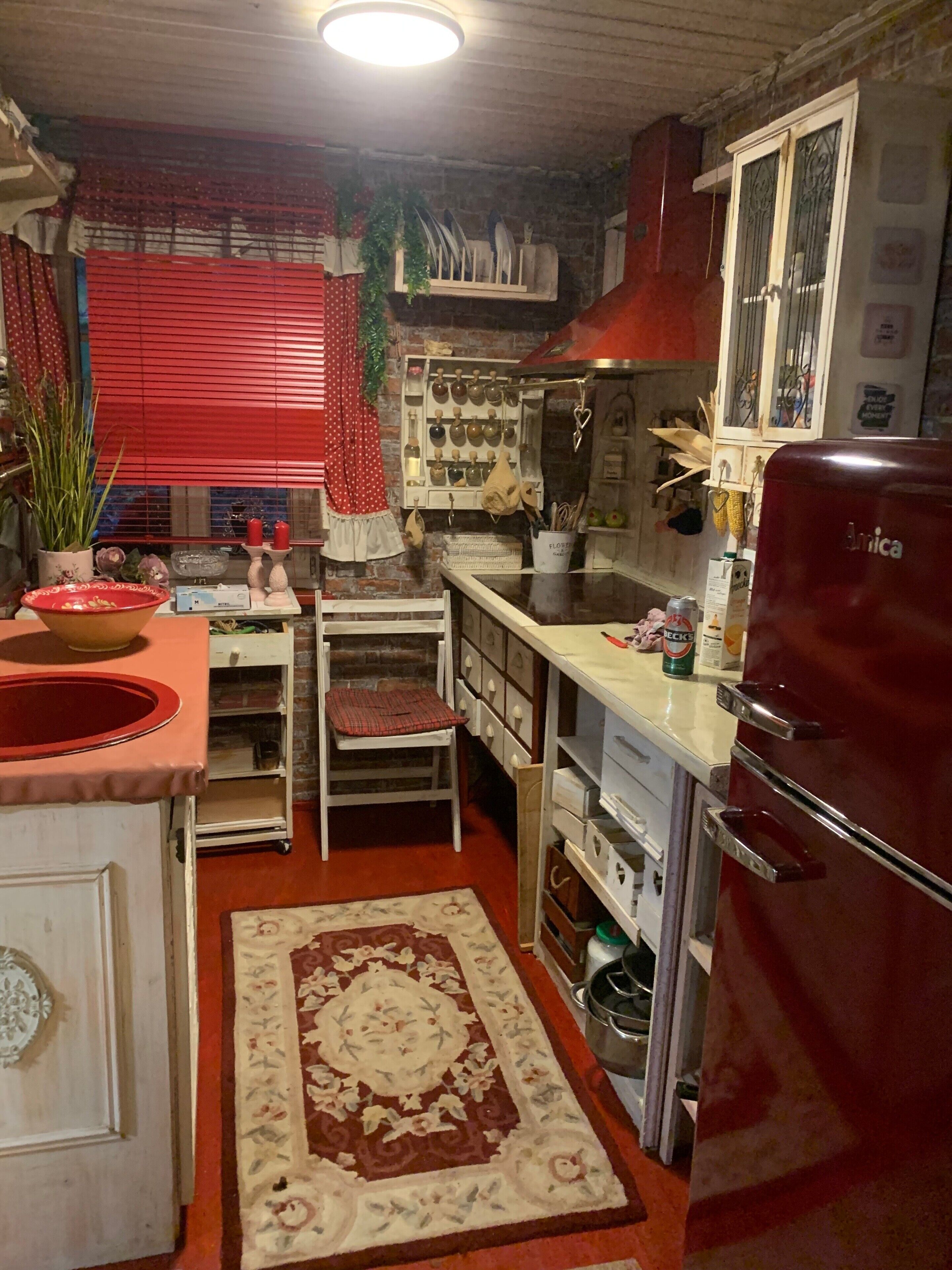 A compact kitchen with a red refrigerator, a white sink, and a red patterned rug.