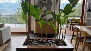 A modern living room with a large window, a dining area, and a decorative plant arrangement. - Stylish, bioclimatic family house (Envigado)