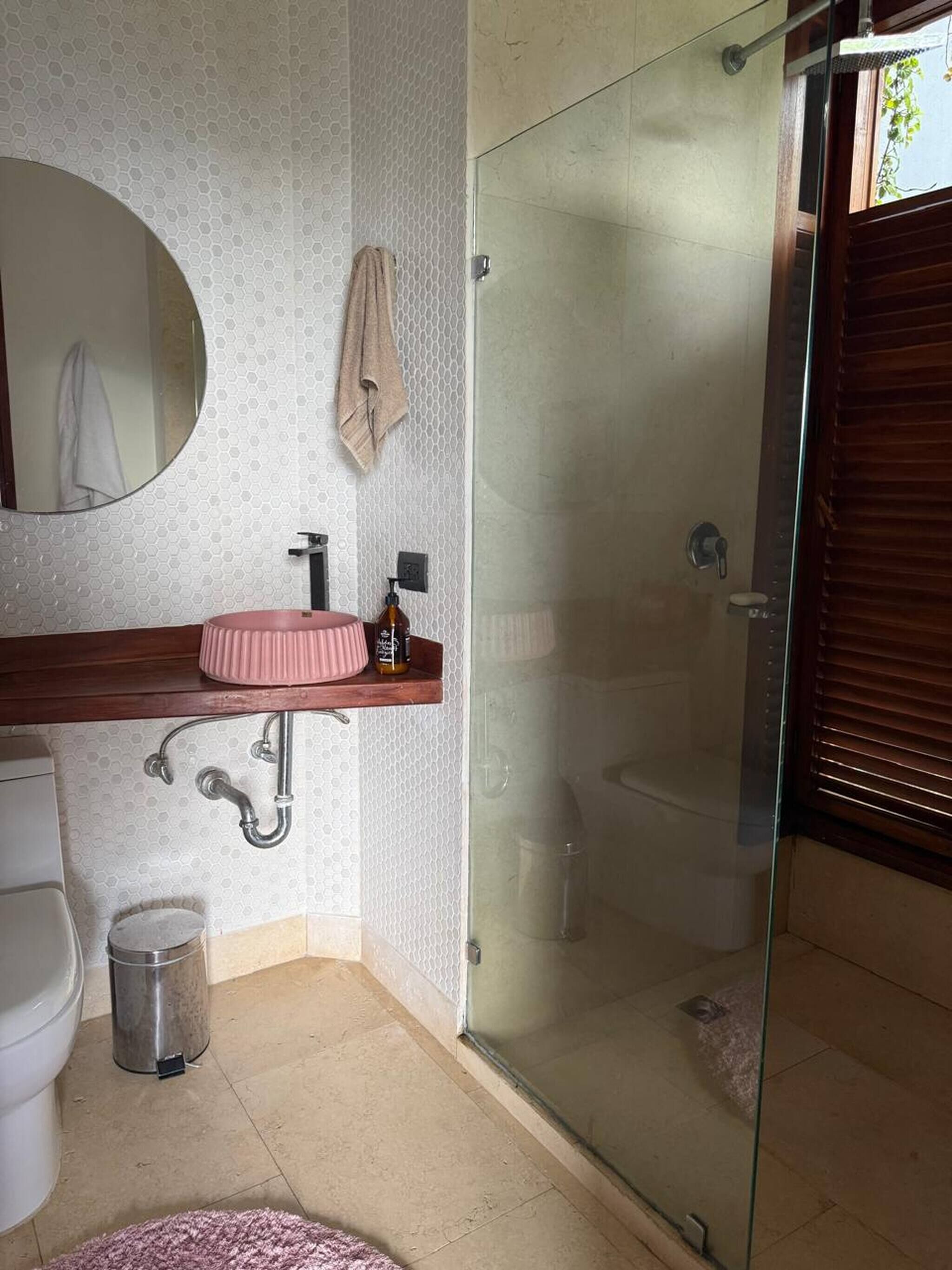 Une salle de bain avec une douche à parois de verre, un miroir rond, un lavabo rose et un porte-serviettes.