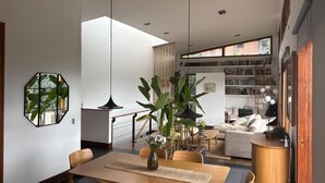 A modern living space with a dining area, a seating area with a sofa and bookshelves, and a large window providing natural light. - Stylish, bioclimatic family house (Envigado)