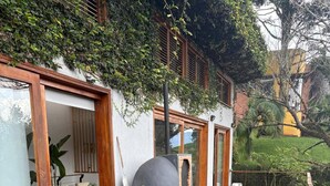 A wooden deck with a table and benches, surrounded by greenery and a building with large windows. - Stylish, bioclimatic family house (Envigado)
