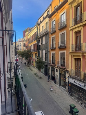 Vista da rua com edifícios, um pedestre e uma fachada comercial com sinalização.