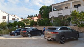 Un’area di parcheggio con tre auto, una persona e un edificio con balconi e vegetazione.