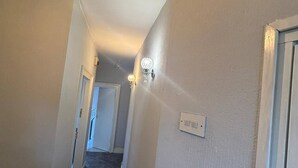 Un pasillo estrecho con piso alfombrado, un interruptor de luz y una lámpara fijada a la pared.