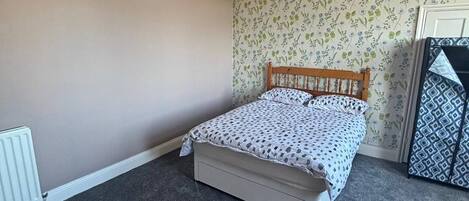 A bedroom with a bed, a radiator, a floral wallpaper, and a hanging light fixture.
