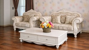 Ein Zimmer mit zwei verzierten Sofas, einem weißen Couchtisch mit floralem Mittelstück und Wandleuchten.