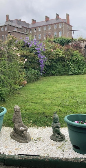 Un jardin avec une pelouse, deux statues de gnomes en pierre et un grand bâtiment en arrière-plan.