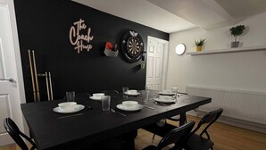 Un coin repas avec une table noire, des assiettes blanches et des chaises noires. Il y a un jeu de fléchettes accroché au mur et une petite plante posée sur une étagère.