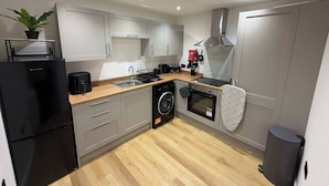 Une cuisine moderne avec des meubles gris, un réfrigérateur noir, un lave-linge, un four et un évier.