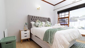 Un dormitorio con cama, mesita de noche, cesto de basura y ventana con vistas.