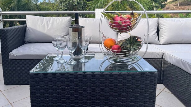 Une table en osier avec un plateau en verre, une bouteille et un panier de fruits.