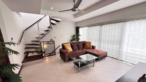 Un salon moderne avec un escalier, un canapé d’angle et un ventilateur de plafond.