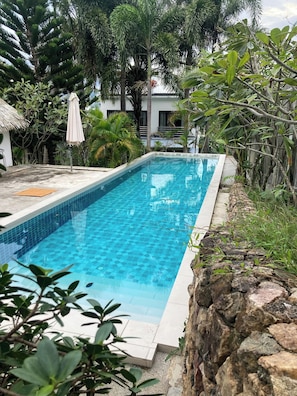 A rectangular swimming pool with clear blue water, surrounded by greenery and a stone wall. - SAMUI SABAI house 4 in the garden with communal pool (Bo Put)