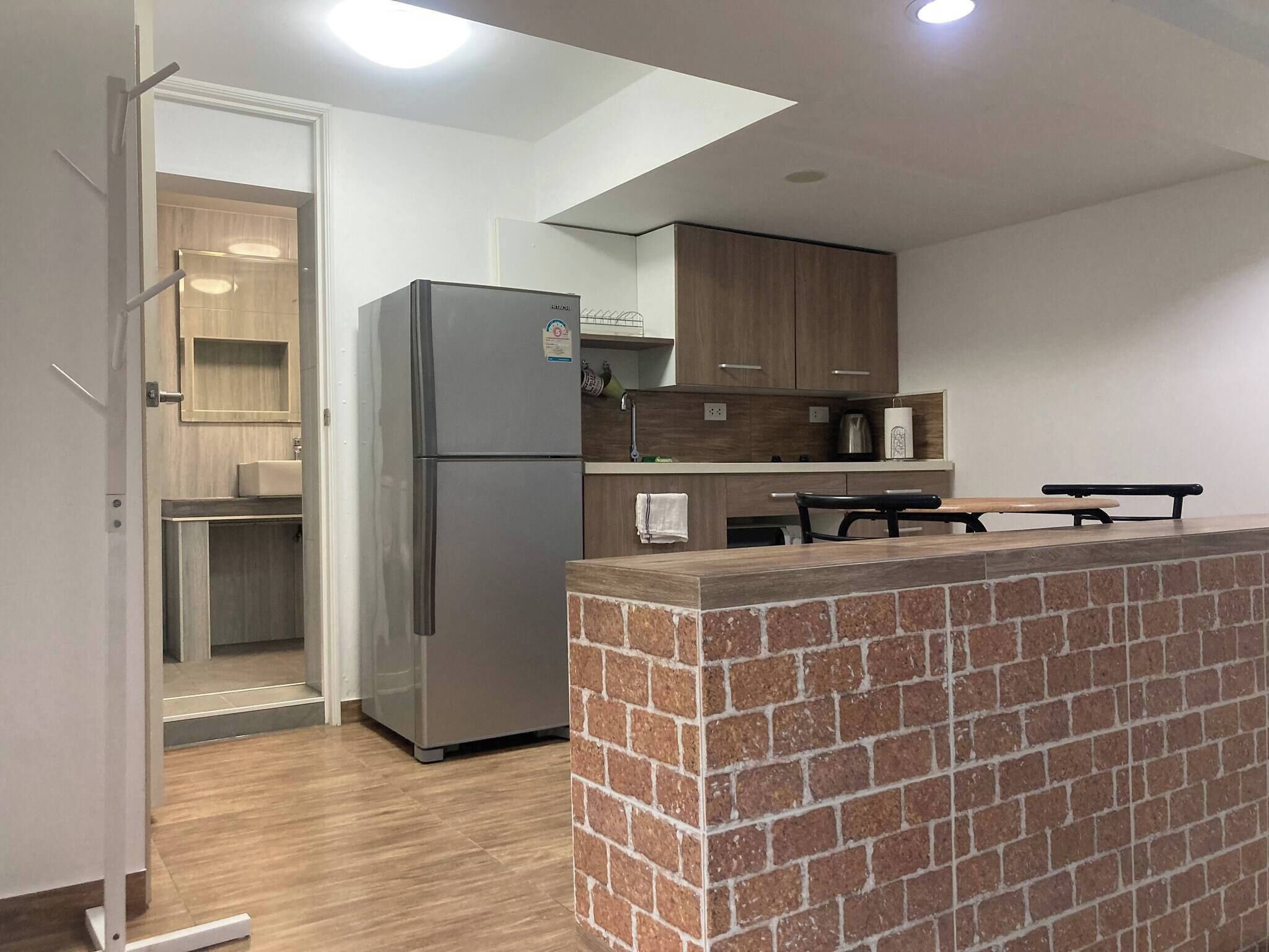 A modern kitchen with a refrigerator, wooden cabinets, a brick accent wall, and a dining area.