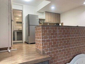Eine Küche mit Kühlschrank, Holzschränken und einer Wand aus Ziegelsteinen.