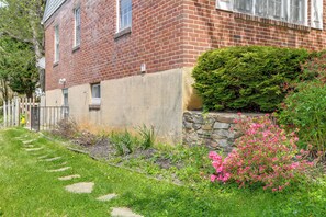 A brick building with a stone retaining wall, a well-maintained garden with stepping stones, and a white picket fence. - Gateway to Downtown Baltimore! Cozy & Private Unit (Baltimore)
