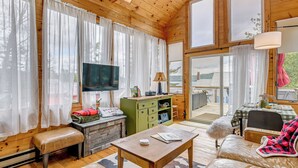 L’intérieur d’un chalet en bois, avec un téléviseur, un meuble vert, un canapé et une vue à travers la porte en verre.