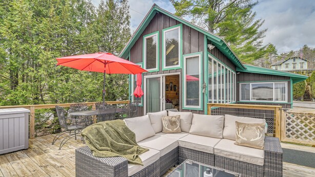 Une terrasse en bois avec des meubles d’extérieur, un parasol rouge et une maison dotée de grandes fenêtres et d’un toit végétalisé.