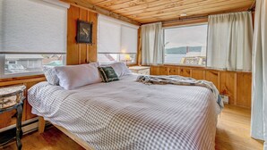 Une chambre à coucher dans une cabane en bois, avec un lit, une table de chevet, une lampe et une fenêtre avec des rideaux.