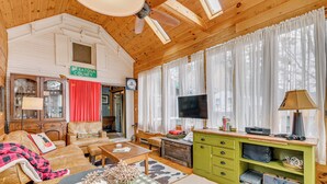 L’intérieur d’un chalet accueillant, avec un canapé, une table à manger, un téléviseur et un meuble vert.