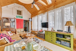 L’intérieur d’un chalet accueillant, avec un canapé, une table à manger, un téléviseur et un meuble vert.