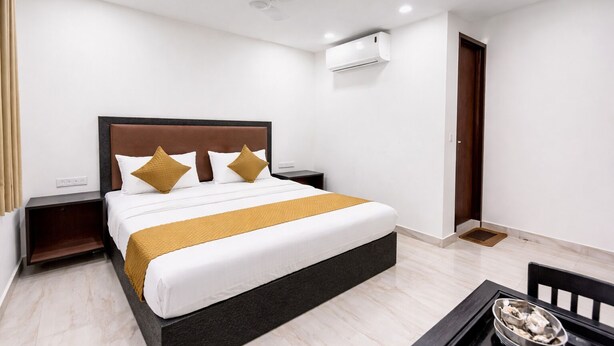 A hotel room with a bed, a nightstand, a bedside table, a ceiling fan, an air conditioning unit, a door, and a small table with a bowl. - Roomshala Kasa Palace (New Delhi)