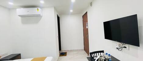 Une chambre d’hôtel comprenant un lit, un bureau avec une chaise, un téléviseur et un appareil de climatisation.