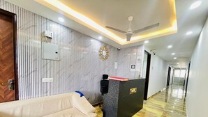 A hotel reception area with a sofa, a reception desk, a ceiling fan, and a corridor leading to other rooms. - Roomshala Kasa Palace (New Delhi)