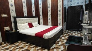 A bedroom with a bed, a desk, a chair, a ceiling fan, and a bathroom with a shower. - Hotel Om Shivay  (Raebareli)