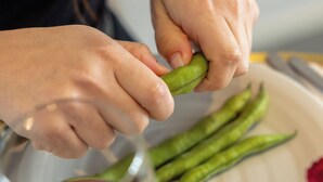 Una persona pelando un vegetal verde, un plato con vegetales verdes y una copa de vino tinto.