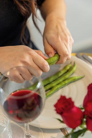 Eine Person schält ein grünes Gemüse, ein Teller mit grünem Gemüse und ein Glas Rotwein.